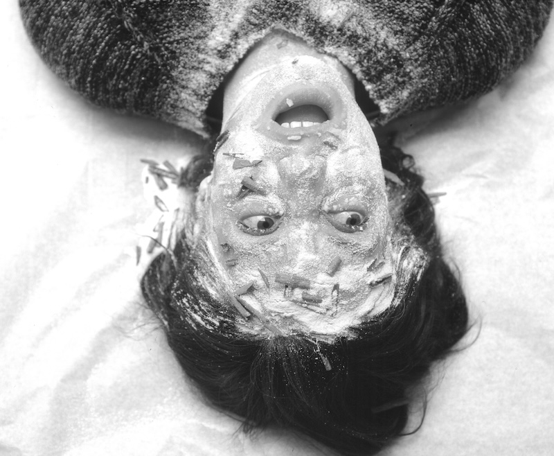 Black & white photograph of a woman laying in the sand with sand in her face