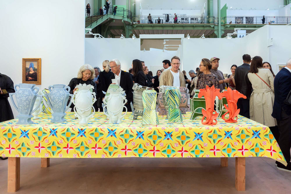 Several vases stanting on a table with a yellow table cloth in a fair booth with many visitors