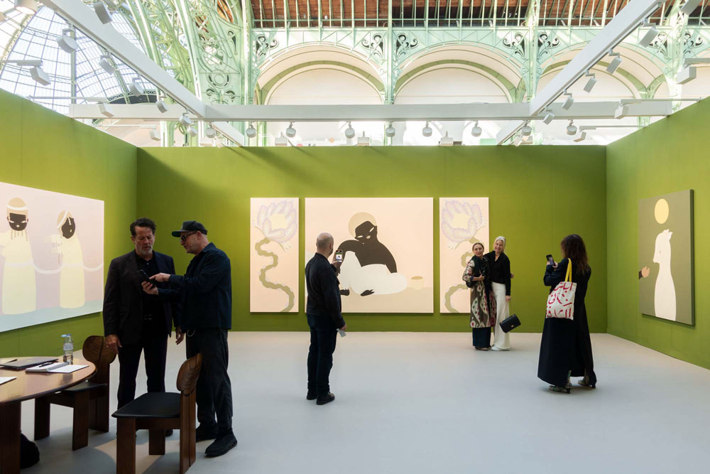 Fair booth green painted walls and visitors, presenting paintings hangin on the walls