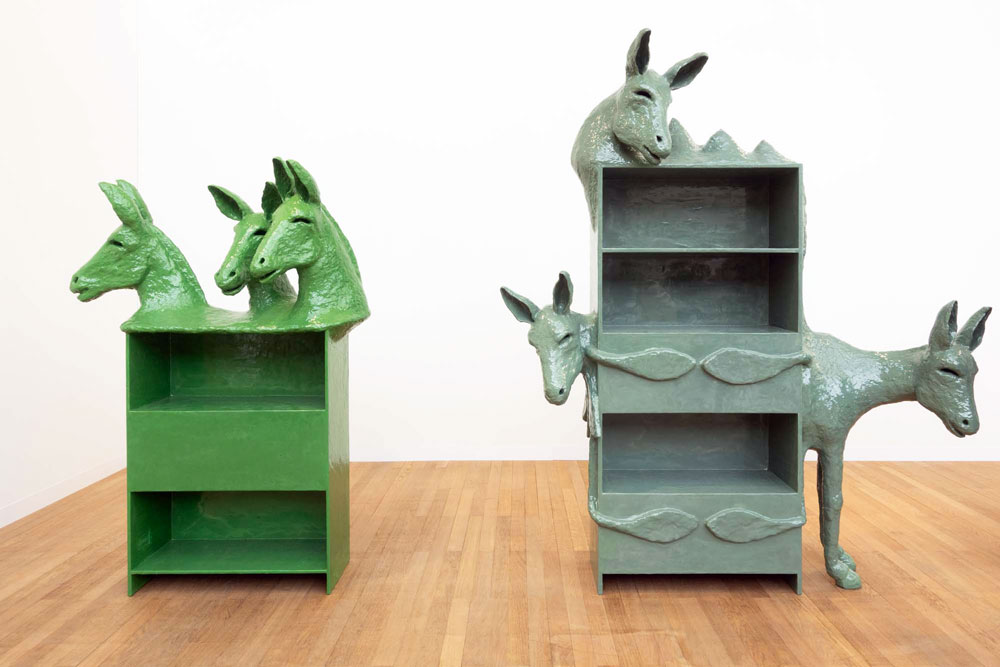 Two sculpture, one green, one gray, each presenting a shelf with donkey heads