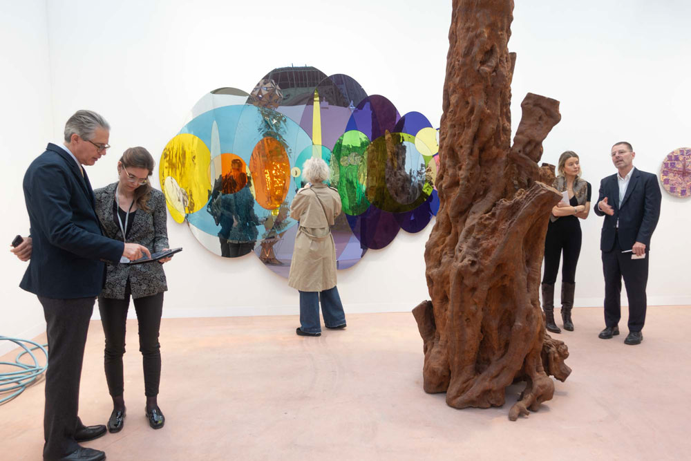 Fair both with a colorful mirroring sculpture, a brown tree sculpture, and gallery staff and visitors