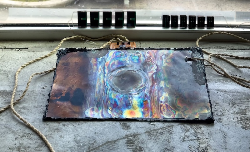 aluminium plate with water in the middle, connected with wires next to a window